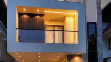 Een modern huis met twee verdiepingen, een balkon, grote ramen en een goed verlichte ingang.