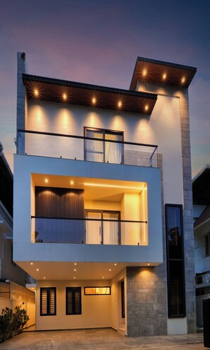 Uma casa moderna de dois andares com varanda, janelas amplas e entrada bem iluminada.