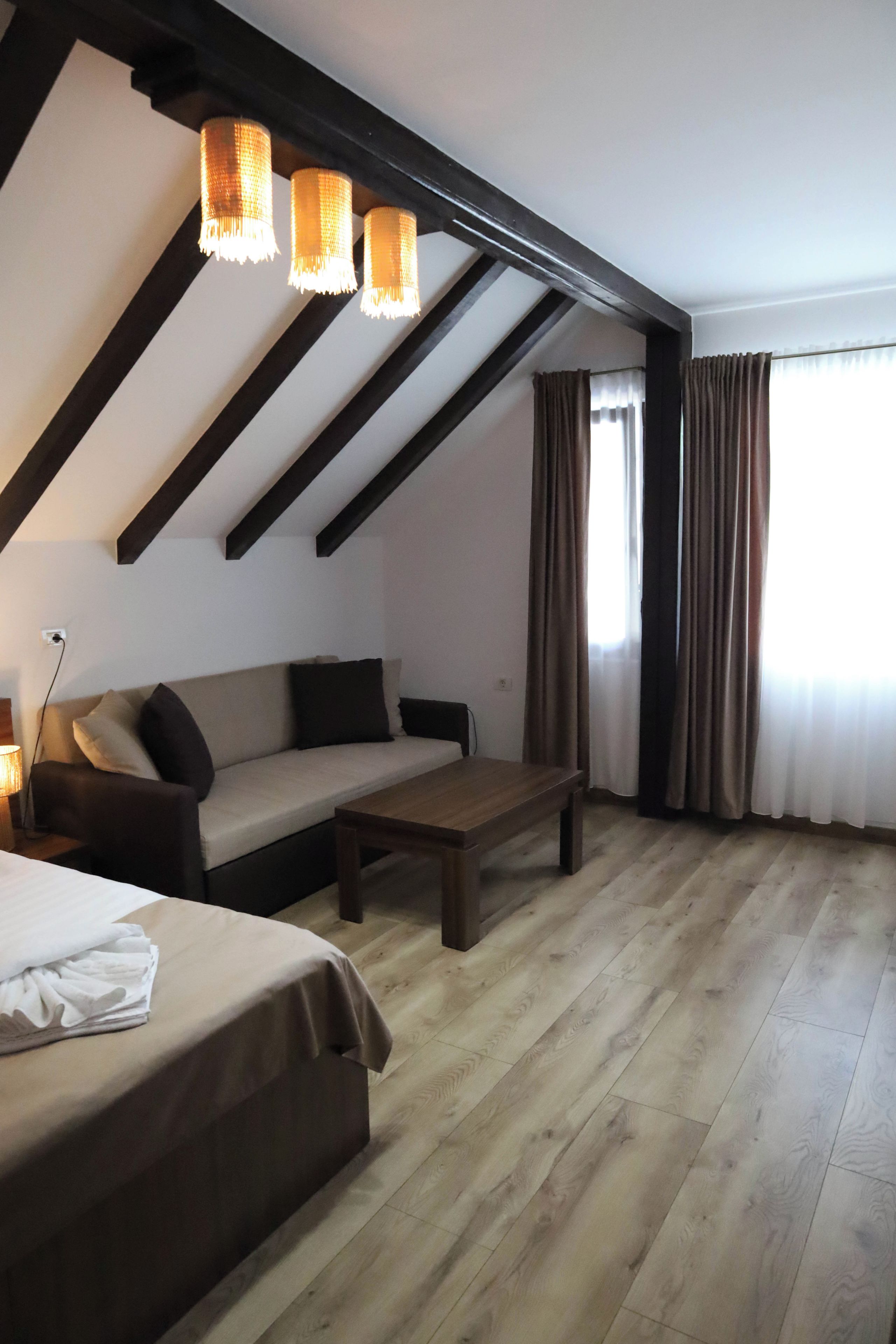 A room with a sofa, a wooden coffee table, a bed with a white cover, and a window with curtains.