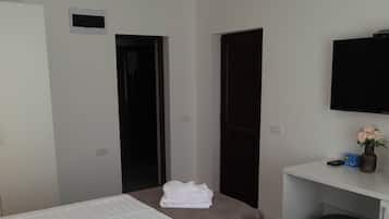 A hotel room with two beds, a desk, a television, and a door.