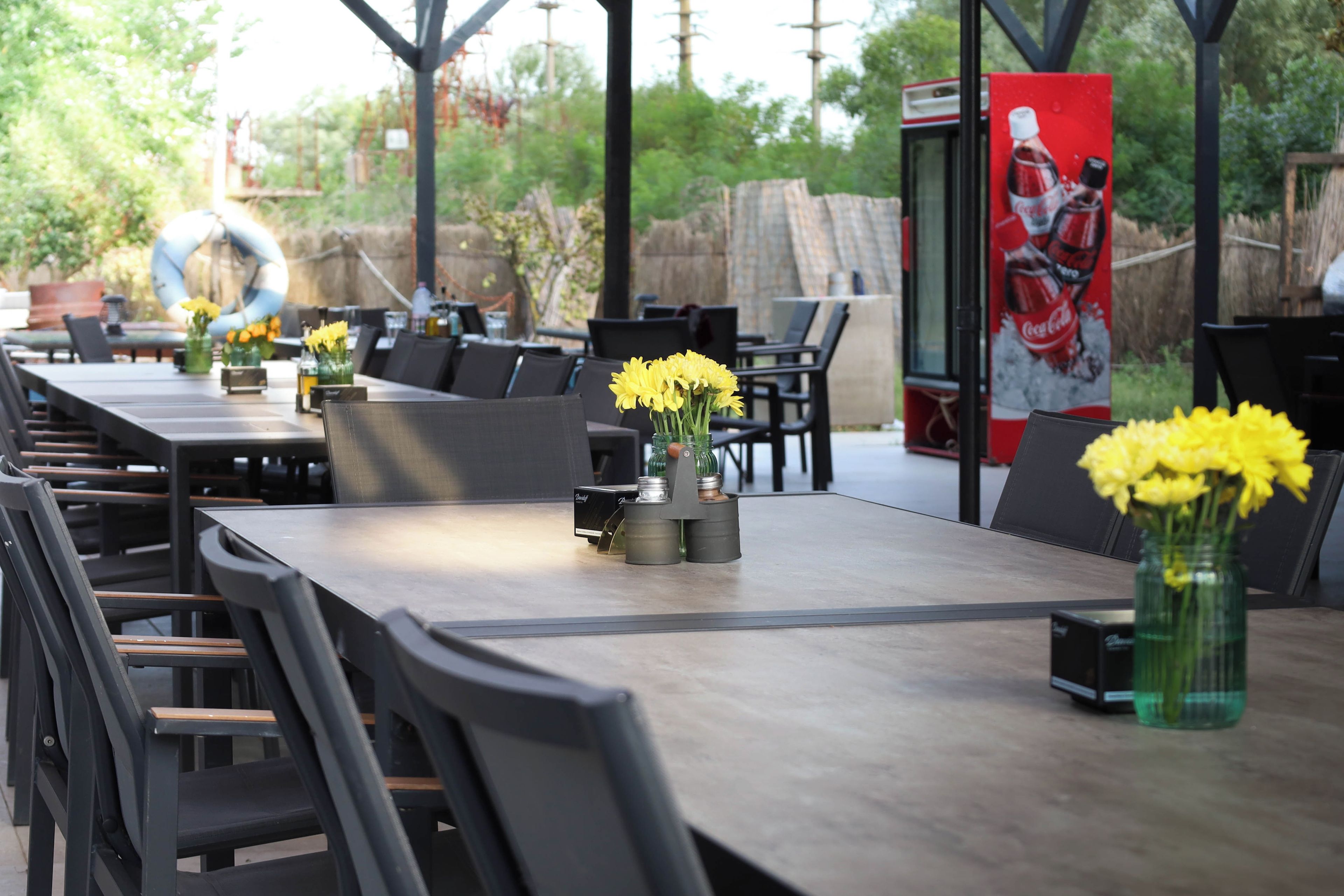 An outdoor dining area with tables and chairs, some with flowers.