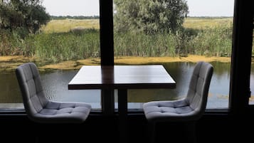 A table with two chairs facing a body of water with vegetation.