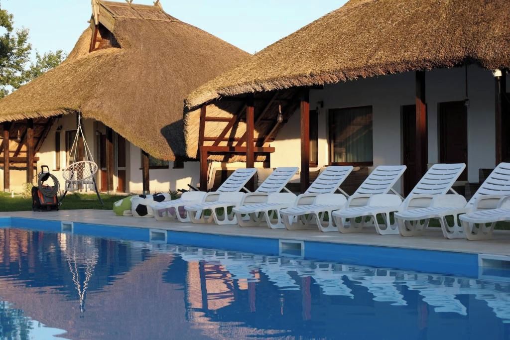 Un área de piscina con sillas de descanso y un edificio con techo de paja.