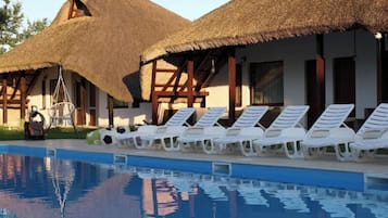 Un área de piscina con sillas de descanso y un edificio con techo de paja.