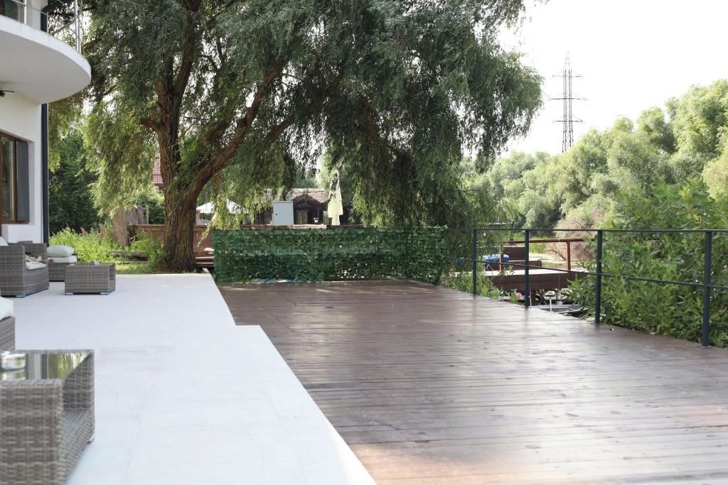 Une terrasse en bois avec des meubles d’extérieur, un grand arbre et une haie.