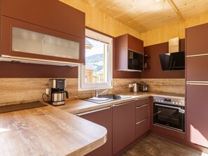 A compact kitchen with wooden cabinets, a built-in microwave, a coffee maker, and a stove. - Cabin With 1 Bedroom (Sankt Georgen am Kreischberg)