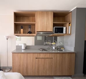 A modern kitchen with wooden cabinets, a microwave, and a stainless steel sink. - Edificio Agustinas by Domus Travels (Santiago)