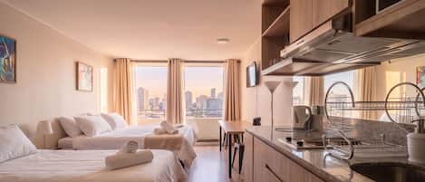 A hotel room with two beds, a kitchenette, and a city view.