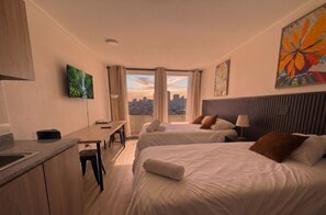 A hotel room with two beds, a desk, a TV, and a city view. - Edificio Agustinas by Domus Travels (Santiago)