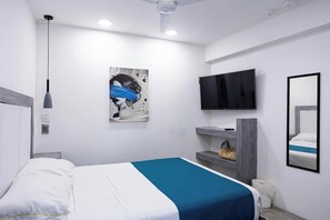 Un dormitorio moderno con cama, televisor montado, un cuadro y ventilador de techo.