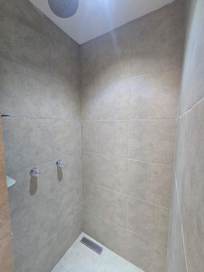 Pequeno banheiro com revestimento de azulejos, ralo e um chuveiro.