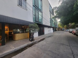 Vista da rua com um restaurante à esquerda, calçada e carros estacionados à direita.