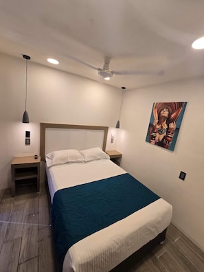 Quarto com cama, duas mesas de cabeceira, ventoinha no teto e uma obra de arte na parede.