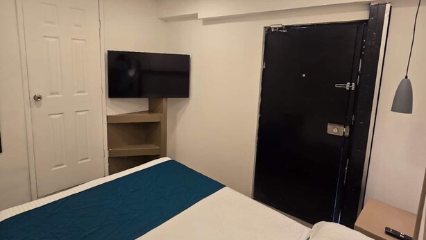 Une chambre à coucher avec un lit, un téléviseur fixé au mur, un ventilateur de plafond et une porte.