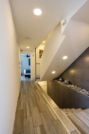 Ein modernes Interieur mit Holzboden, einer Treppe an einer dunklen Wand und einer Decke mit eingelassener Beleuchtung.
