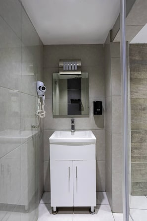 Casa de banho moderna com toucador branco, espelho, secador de cabelo e dispensador de sabonete.