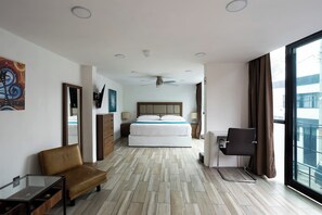 Quarto de hotel com cama, escrivaninha, cadeira, televisão e uma janela grande.