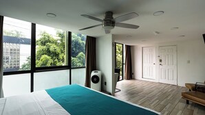 Une chambre moderne avec un grand lit, un ventilateur de plafond, une fenêtre donnant sur un espace verdoyant et une porte menant à un espace extérieur.
