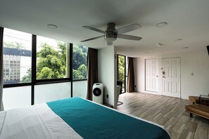 Quarto moderno com cama grande, ventilador de teto, janela vista para vegetação e porta que dá para área externa.