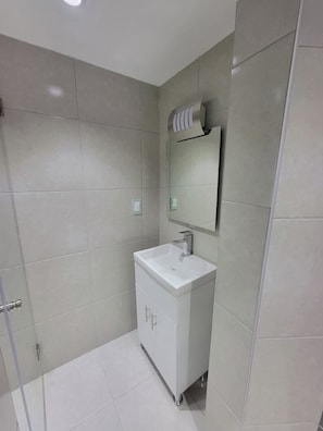 Casa de banho com lavatório branco, espelho e zona de duche.