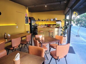 Interior de café com mesas e cadeiras de madeira, área de bar e vista para a rua.