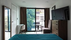 Une chambre avec un lit, un bureau, une chaise, une télévision et une porte coulissante donnant sur un balcon.