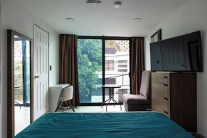 Quarto com cama, escrivaninha, cadeira, televisão e porta de correr para uma varanda.