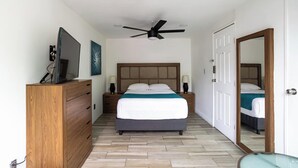 Une chambre d’hôtel avec un lit, une commode en bois, un téléviseur et un ventilateur de plafond.