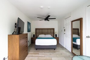 Quarto de hotel com uma cama, penteadeira de madeira, televisão e ventoinha no teto.