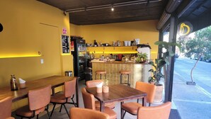 L’intérieur d’un café, avec des tables et des chaises en bois, un comptoir et une vue sur la rue.