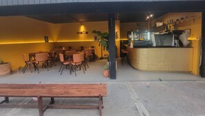 Un espace extérieur aménagé avec des tables et des chaises, un comptoir avec une machine à café et une enseigne sur laquelle on peut lire « MODO ».