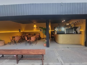 Uma área externa com mesas e cadeiras, um balcão com uma máquina de café e uma placa com a inscrição 'MODO'.