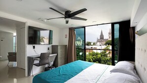 Une chambre d’hôtel avec un lit, un bureau et une vue sur une cathédrale, visible à travers de grandes fenêtres.