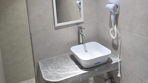 Une salle de bain avec un lavabo blanc, un miroir et un sèche-cheveux fixé au mur.