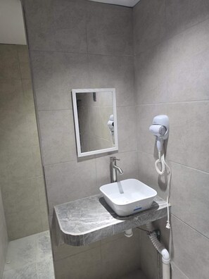 Casa de banho com lavatório branco, espelho e secador de cabelo fixado na parede.