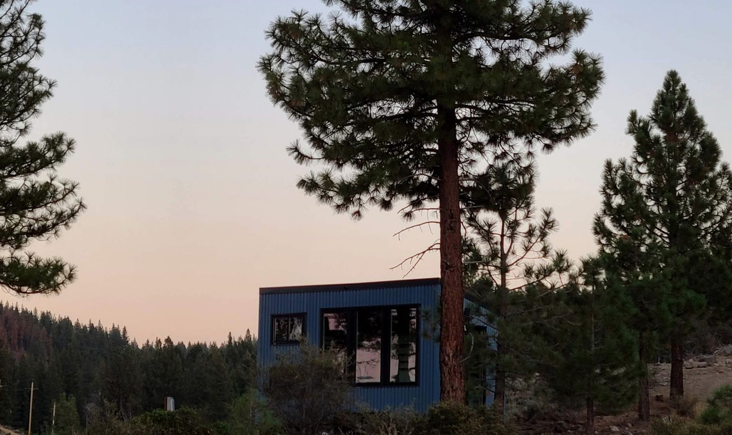 Un pequeño edificio de una sola planta con fachada azul, rodeado de un bosque denso.