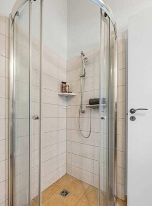 A glass-enclosed shower stall with a handheld showerhead, a towel rack, and a small shelf with toiletries. - Holiday Home With 1 Bedroom (Braunlage)