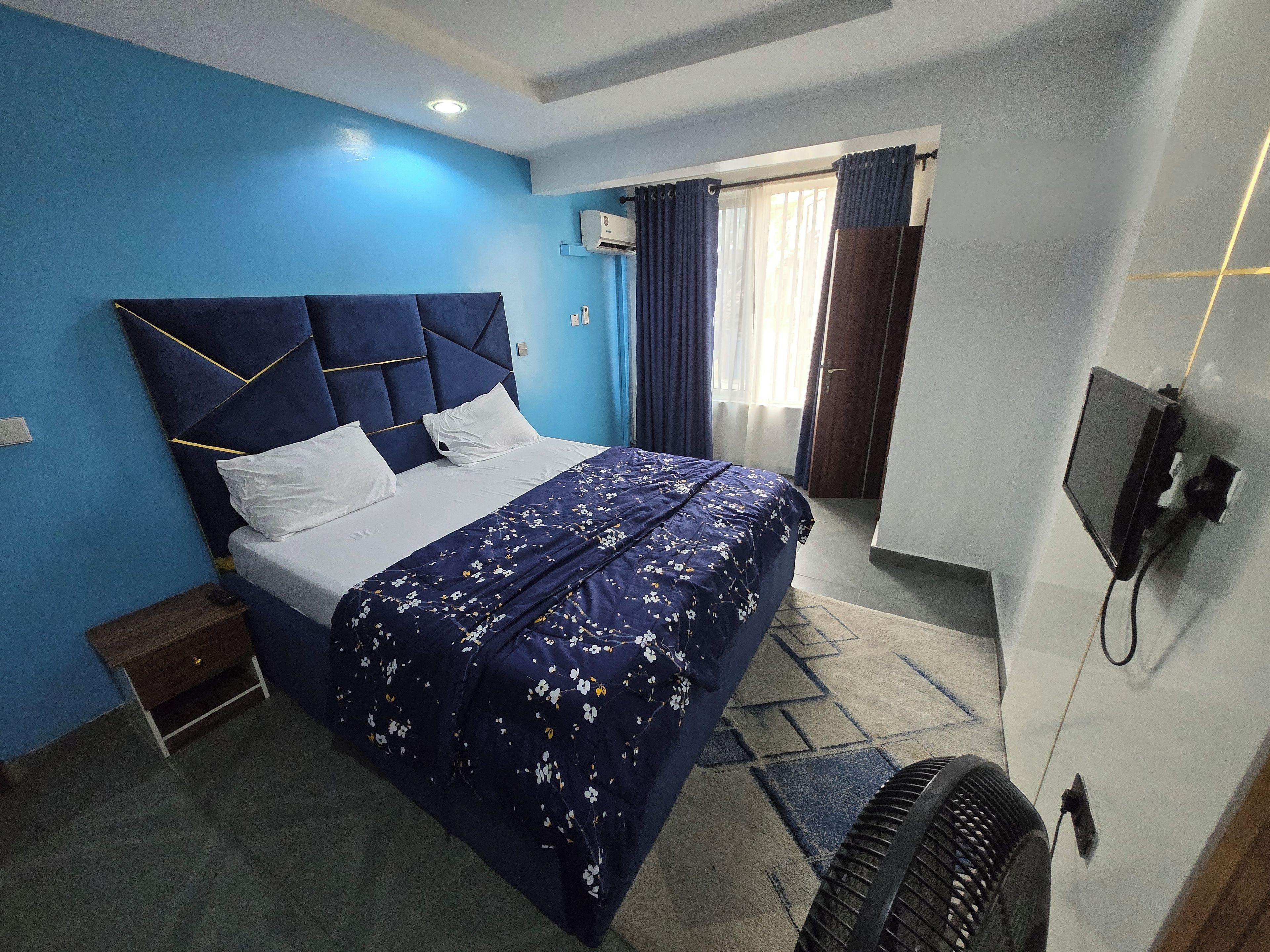 A hotel room with a bed, a bedside table, a TV, and a window with curtains.