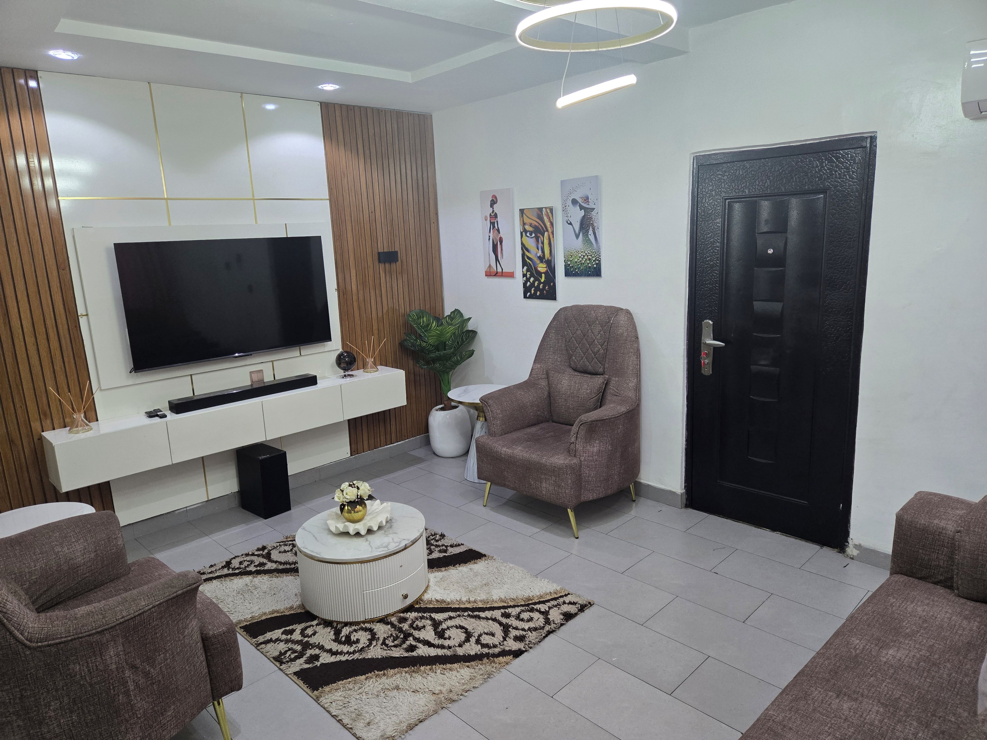 A modern living room with a flat-screen TV, a sofa, a chair, a decorative rug, and a door.