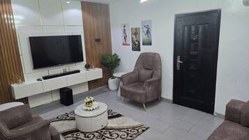 A modern living room with a flat-screen TV, a sofa, a chair, a decorative rug, and a door.