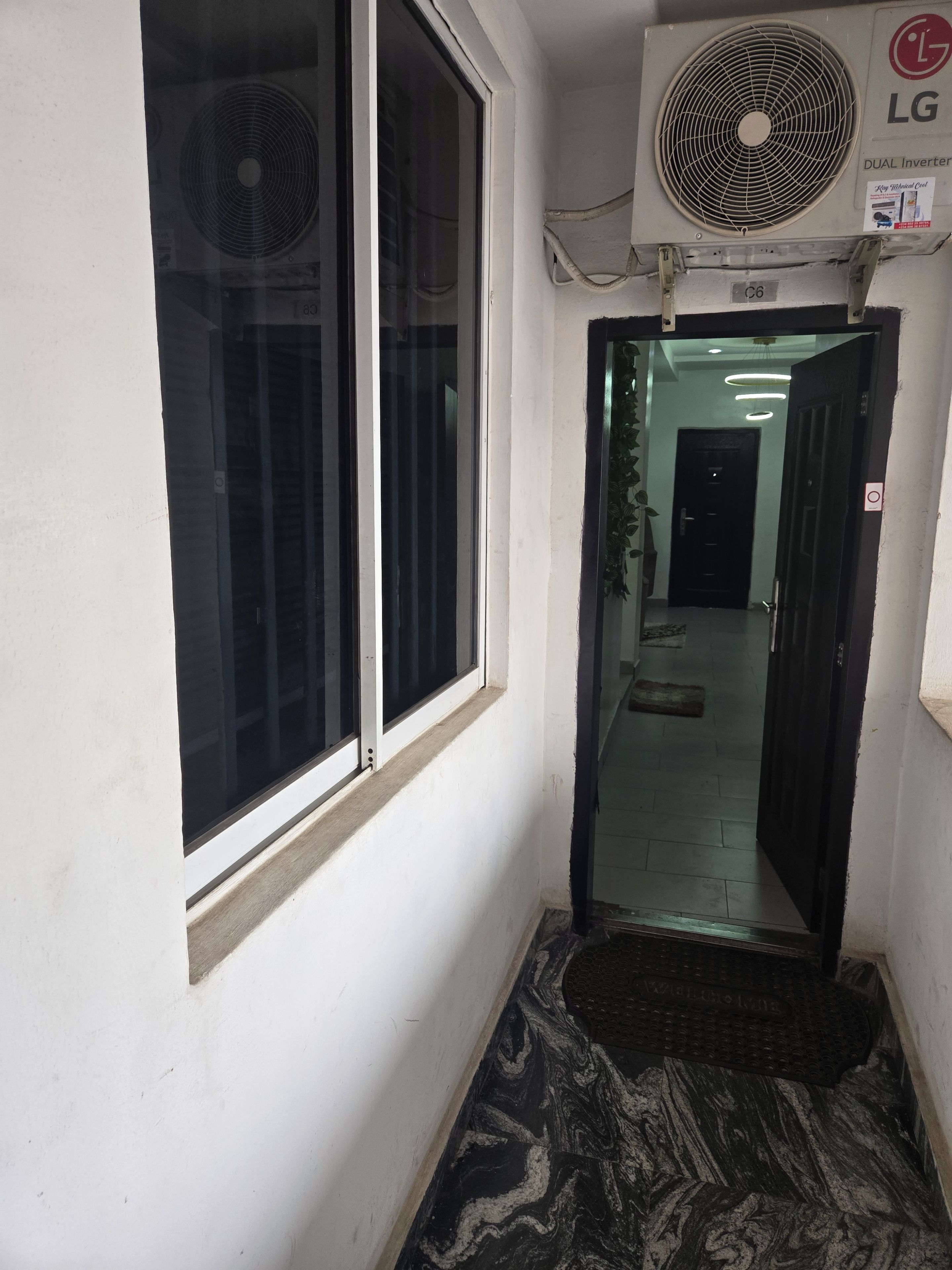 A narrow hallway with a black mat at the entrance, a door leading to a room, and an air conditioning unit mounted on the wall.