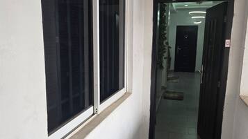 A narrow hallway with a black mat at the entrance, a door leading to a room, and an air conditioning unit mounted on the wall.