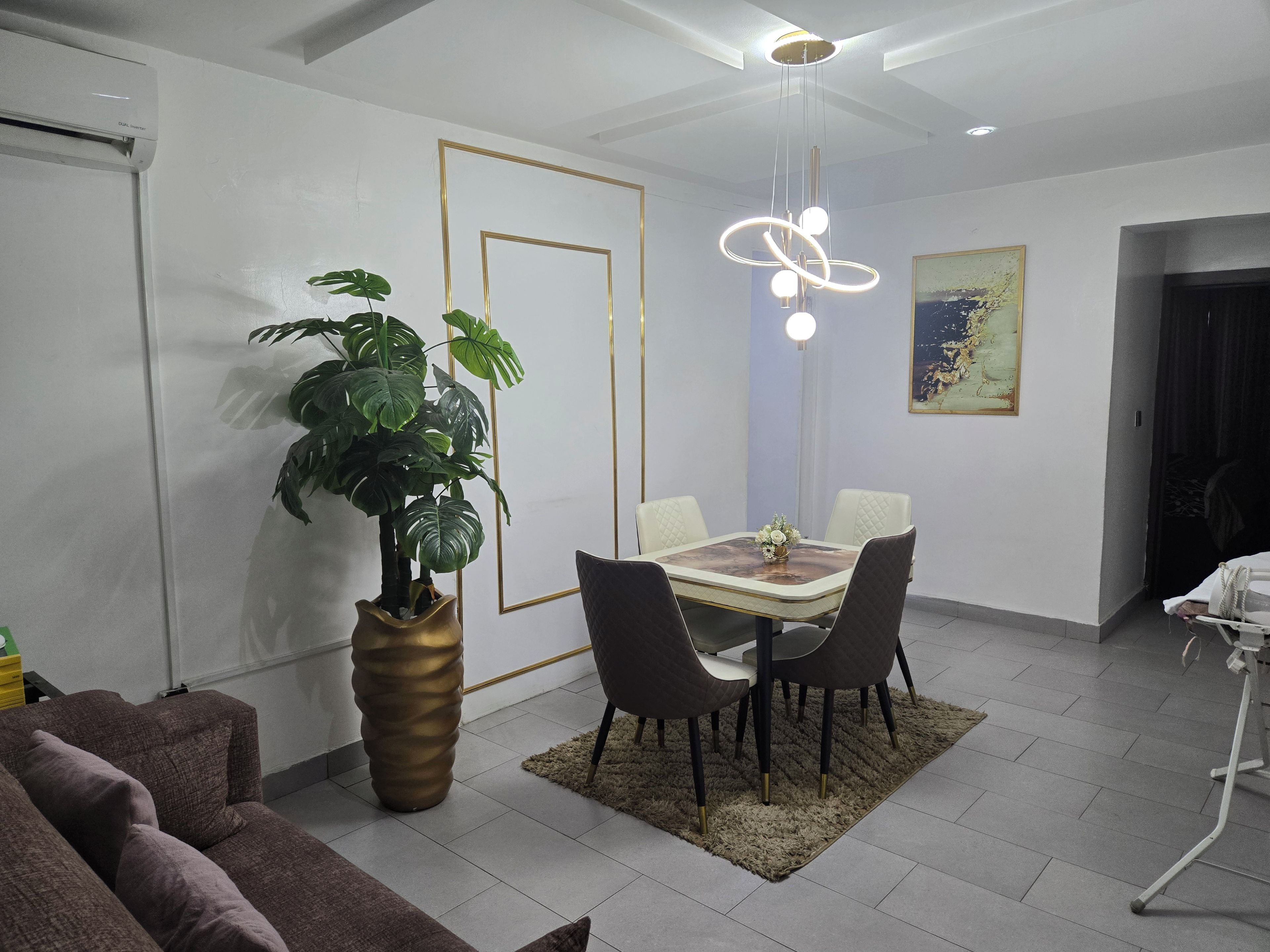 Una zona de menjador amb taula, cadires, una planta i un llum modern.