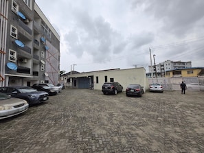 Un estacionamiento con varios autos, un edificio con garaje y una persona caminando.