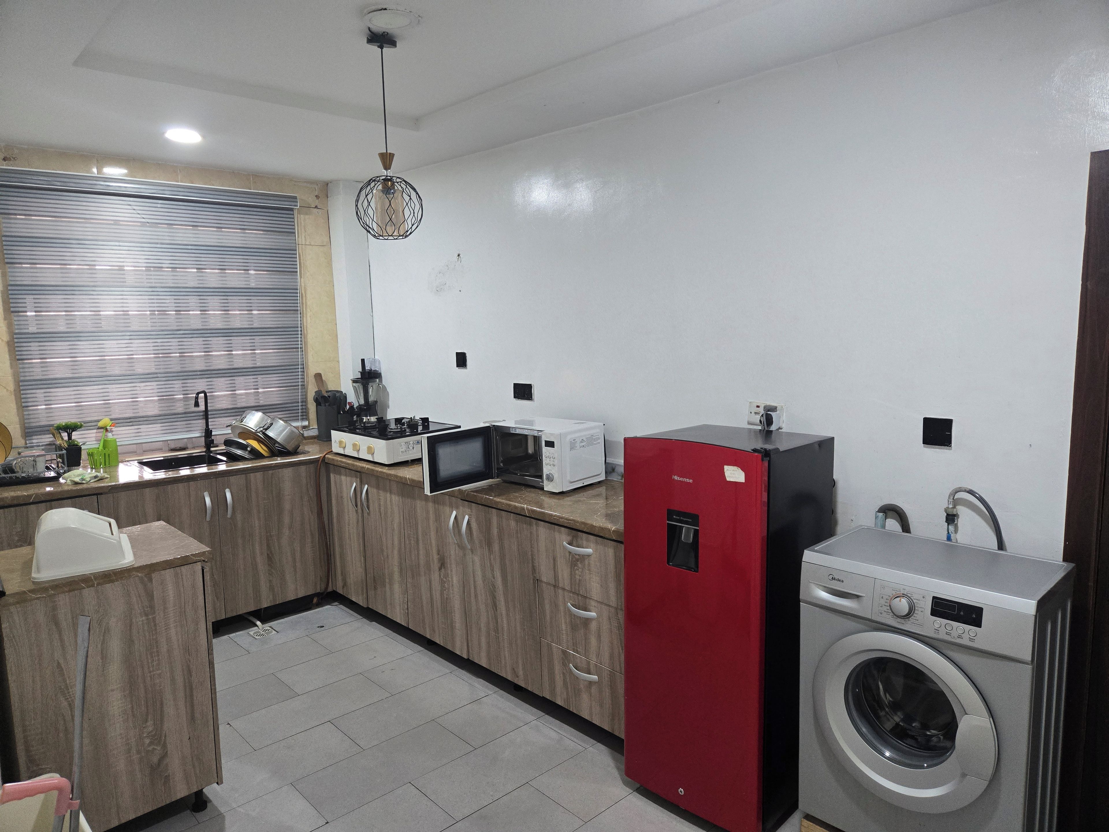 A compact kitchen with a microwave, stove, sink, and a red appliance, likely a refrigerator or freezer.