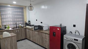 A compact kitchen with a microwave, stove, sink, and a red appliance, likely a refrigerator or freezer.