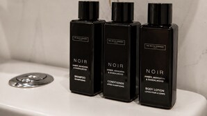 Tre flaconi neri di prodotti per la cura del corpo NOIR su un ripiano bianco in bagno.