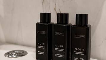 Three black bottles of NOIR body care products on a white bathroom counter.