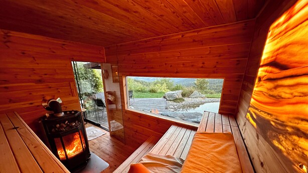 Interior acogedor de una cabaña con chimenea, un banco y una ventana con vistas a un paisaje natural.