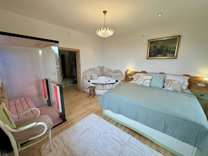 Un dormitorio con una cama, una silla, una bañera y un cuadro en la pared.